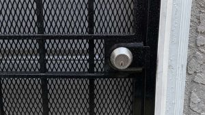 Silver deadbolt on a rain-covered black metal security gate in Hackettstown, NJ