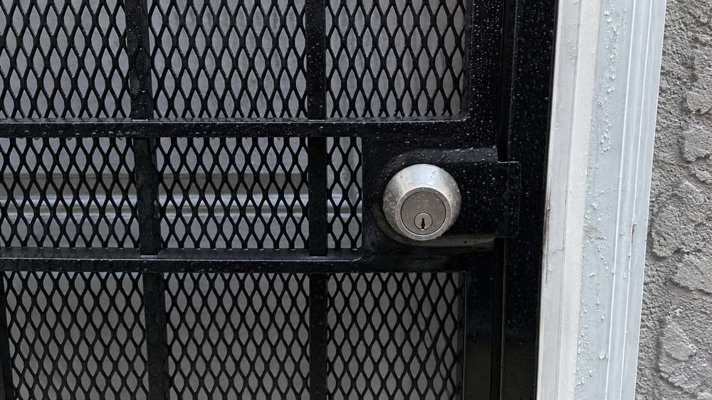 Silver deadbolt on a rain-covered black metal security gate in Hackettstown, NJ